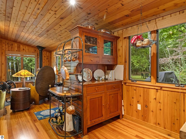 kitchen featuring wood walls, wooden ceiling, a wood stove, vaulted ceiling, and light hardwood / wood-style floors