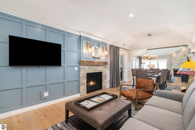 living room featuring vaulted ceiling, a stone fireplace, a chandelier, and light hardwood / wood-style flooring