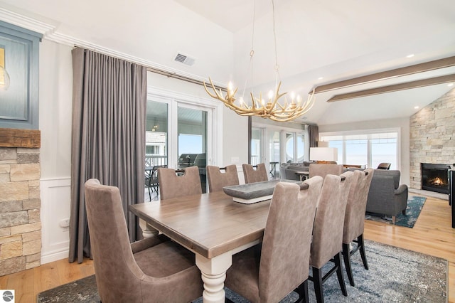 dining space featuring lofted ceiling with beams, hardwood / wood-style floors, a stone fireplace, and a notable chandelier