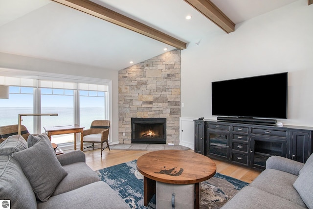 living room with vaulted ceiling with beams, light wood-type flooring, and a stone fireplace