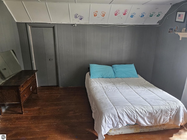 bedroom with wooden walls, a closet, and dark hardwood / wood-style floors