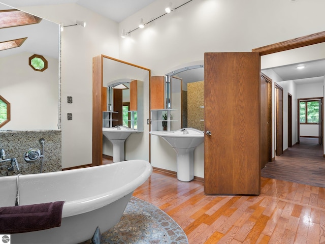 bathroom featuring a tub to relax in, tasteful backsplash, hardwood / wood-style floors, and double sink