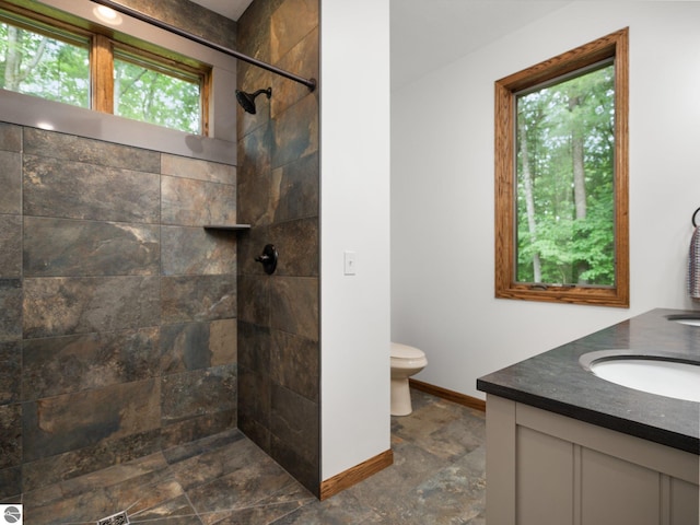 bathroom featuring a tile shower, vanity, a healthy amount of sunlight, and toilet