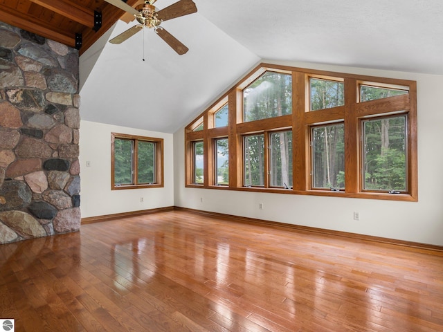 unfurnished living room with wood-type flooring, vaulted ceiling with beams, a wealth of natural light, and ceiling fan