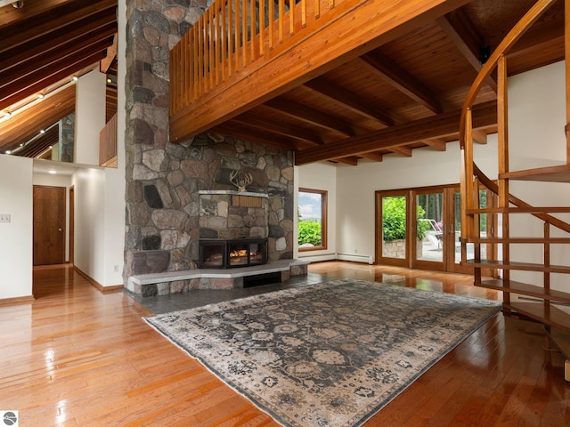 living room featuring light wood-type flooring, a towering ceiling, beam ceiling, wooden ceiling, and a stone fireplace