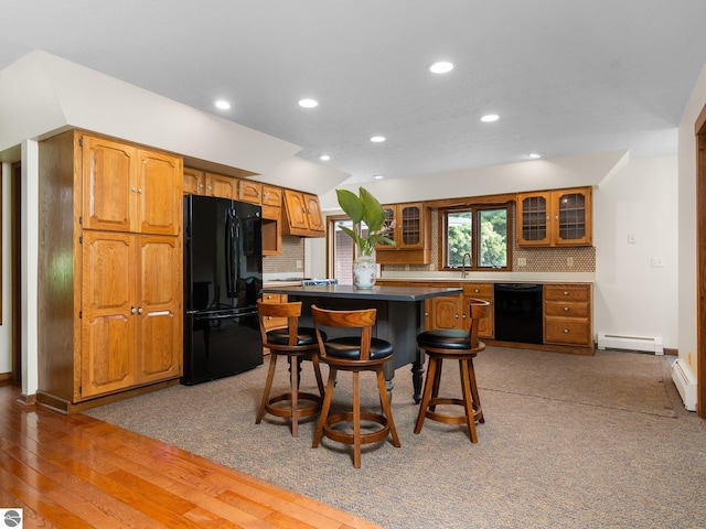 kitchen featuring black appliances, backsplash, baseboard heating, and a breakfast bar area