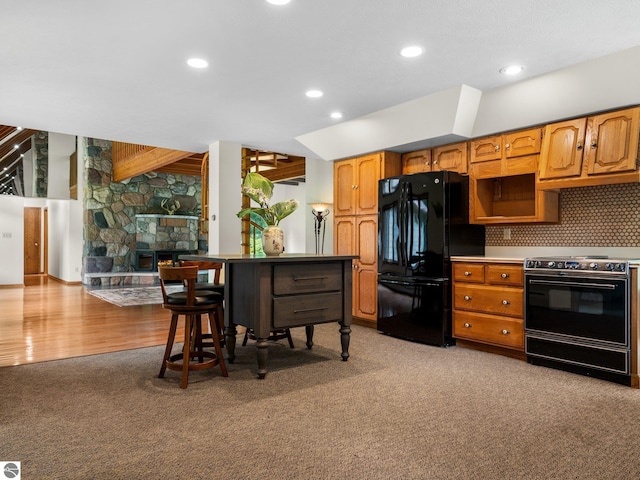 kitchen with range with electric stovetop, black fridge, a stone fireplace, and light carpet