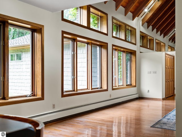 unfurnished room featuring brick ceiling, vaulted ceiling with beams, light hardwood / wood-style flooring, and a baseboard heating unit