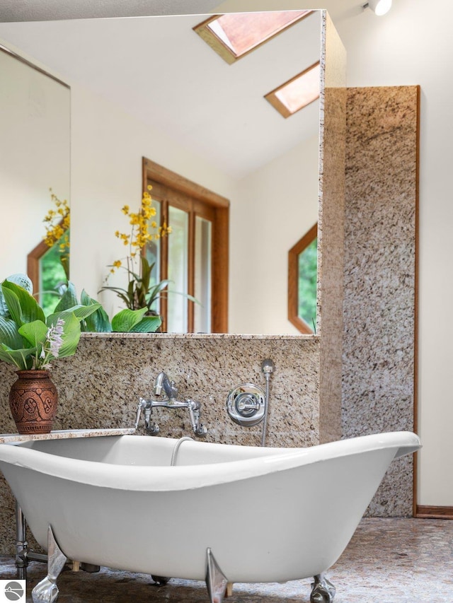 bathroom with a tub to relax in, lofted ceiling with skylight, and sink