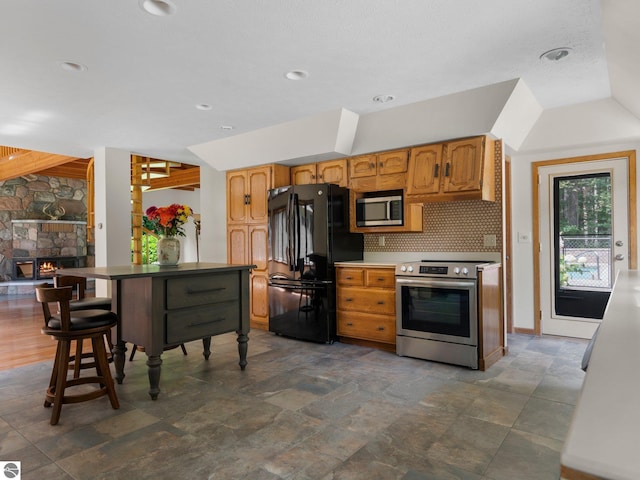 kitchen with a fireplace, decorative backsplash, stainless steel appliances, and a kitchen breakfast bar