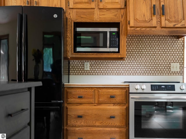 kitchen featuring decorative backsplash, black refrigerator, and stove