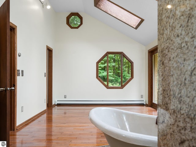 bathroom with a bathing tub, hardwood / wood-style flooring, vaulted ceiling with skylight, and a baseboard heating unit