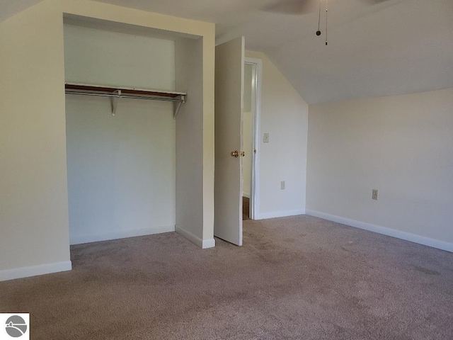 unfurnished bedroom featuring a closet, light colored carpet, vaulted ceiling, and ceiling fan