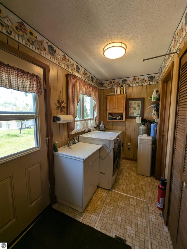 clothes washing area featuring cabinets, a textured ceiling, independent washer and dryer, and wooden walls