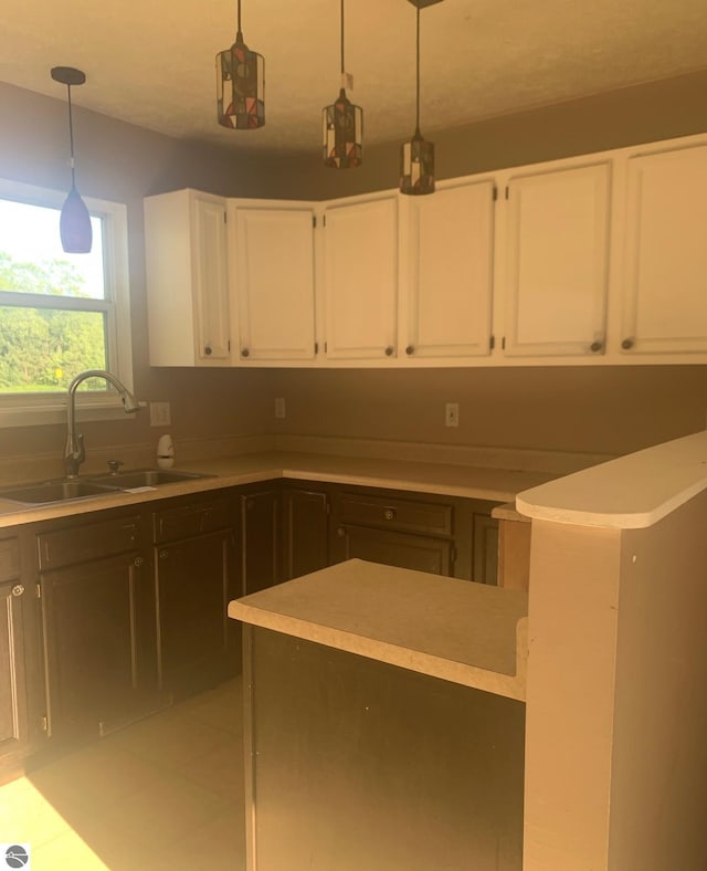 kitchen featuring hanging light fixtures, light tile patterned floors, sink, and white cabinetry