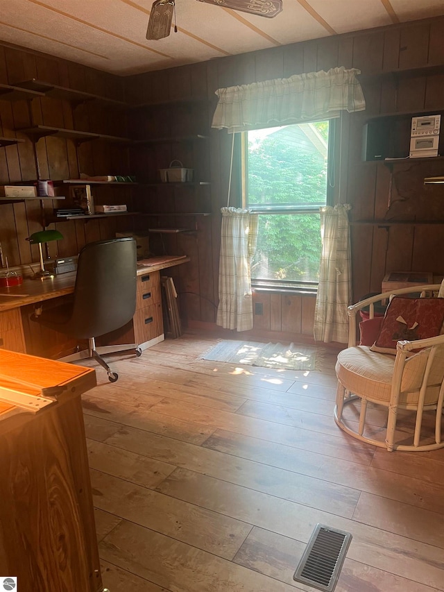 home office featuring light hardwood / wood-style floors, wood walls, and ceiling fan