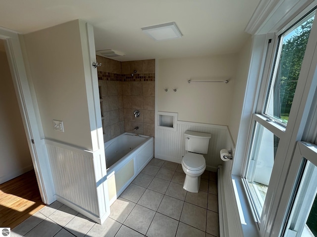 bathroom with toilet, tile patterned floors, tiled shower / bath, and plenty of natural light