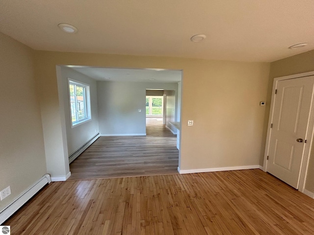 empty room with a baseboard radiator, plenty of natural light, and wood-type flooring