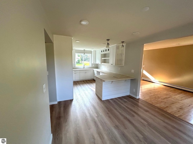 kitchen featuring white cabinetry, hardwood / wood-style flooring, sink, a baseboard radiator, and kitchen peninsula