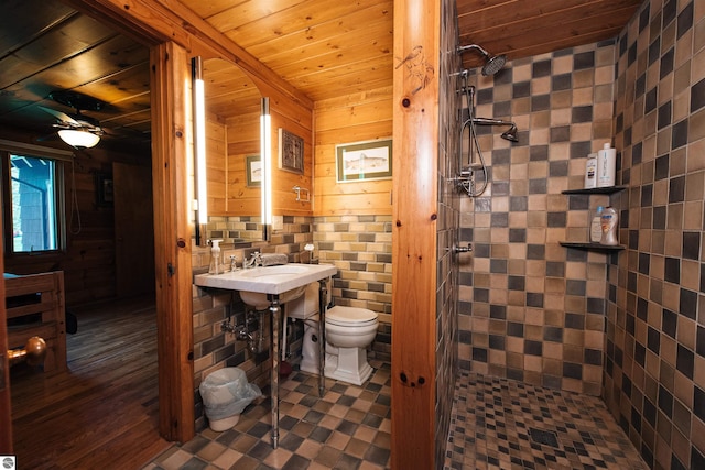 bathroom featuring hardwood / wood-style flooring, wooden walls, a tile shower, toilet, and wood ceiling