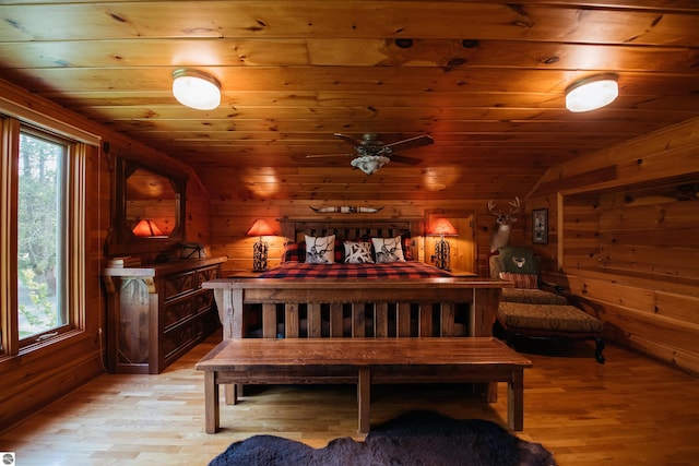 bedroom featuring light hardwood / wood-style flooring, wooden walls, and multiple windows