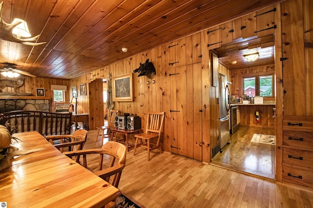 dining room featuring wood walls, wooden ceiling, ceiling fan, and light wood-type flooring