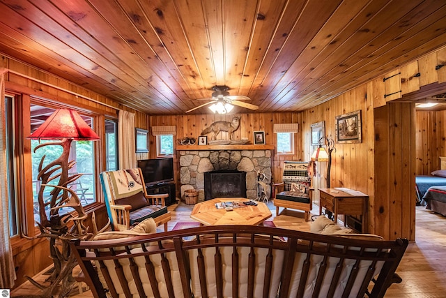 living room featuring wood walls, light hardwood / wood-style flooring, a fireplace, and ceiling fan