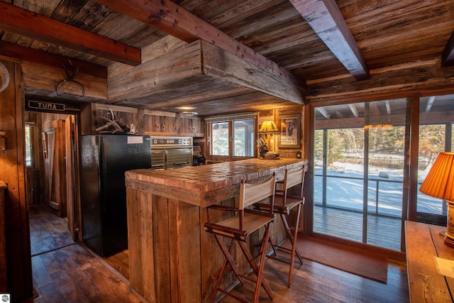 kitchen featuring oven, hardwood / wood-style flooring, black refrigerator, and beam ceiling