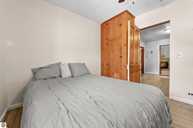 224 Saint Marys St, Suttons Bay, MI 49682 - bedroom featuring a ceiling fan, baseboards, light wood-type flooring, and a warm lit fireplace
