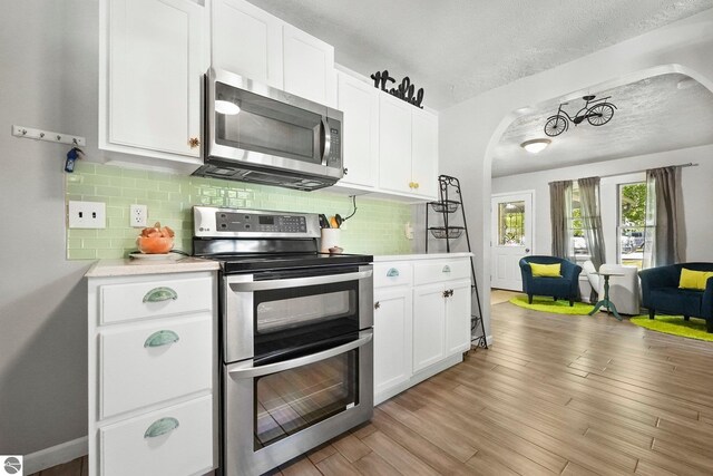 224 Saint Marys St, Suttons Bay, MI 49682 - kitchen featuring arched walkways, light countertops, light wood-style floors, appliances with stainless steel finishes, and tasteful backsplash