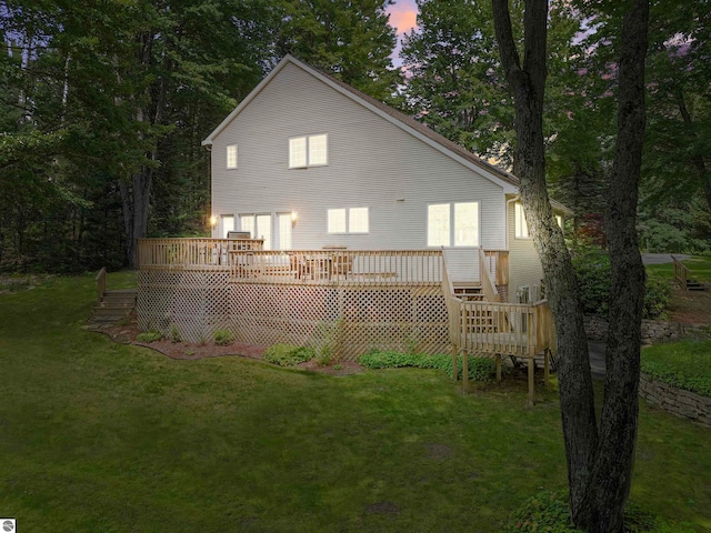 back house at dusk featuring a deck and a lawn