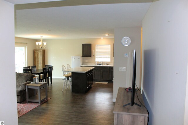 kitchen with dark wood-type flooring, a kitchen breakfast bar, a notable chandelier, and a center island