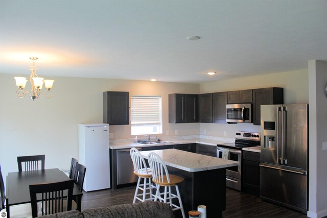 kitchen featuring stainless steel appliances, a breakfast bar, sink, a chandelier, and dark wood-type flooring