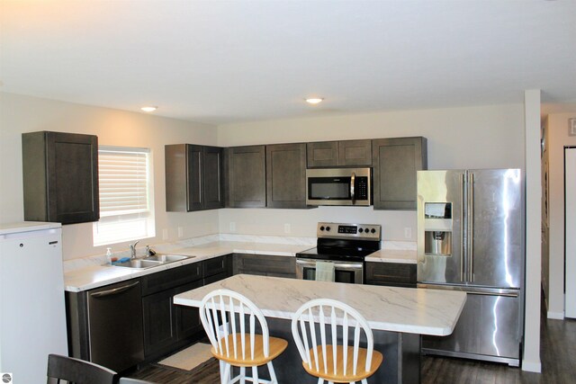 kitchen with dark hardwood / wood-style flooring, a kitchen island, stainless steel appliances, a kitchen breakfast bar, and sink