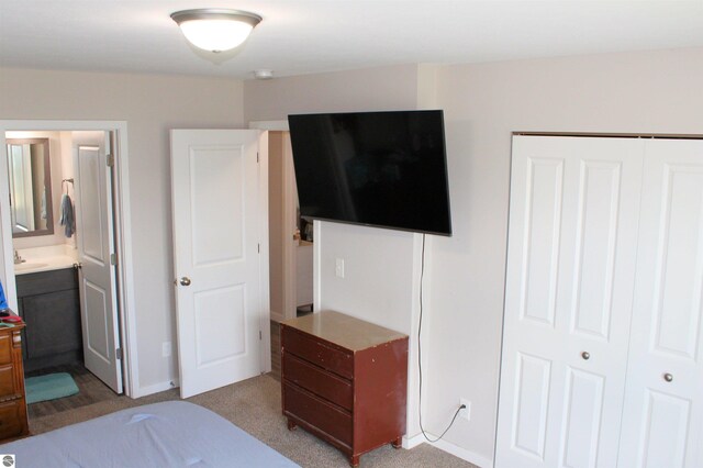 bedroom featuring ensuite bathroom, sink, light carpet, and a closet