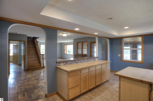 kitchen featuring butcher block counters, a kitchen island, light brown cabinetry, a raised ceiling, and light parquet flooring