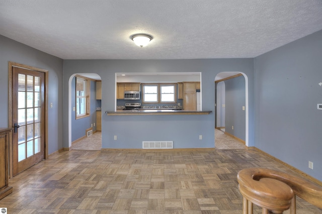 kitchen featuring stainless steel appliances, light parquet floors, a textured ceiling, and kitchen peninsula