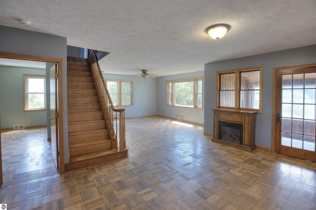 unfurnished living room featuring dark parquet flooring, ceiling fan, and a textured ceiling