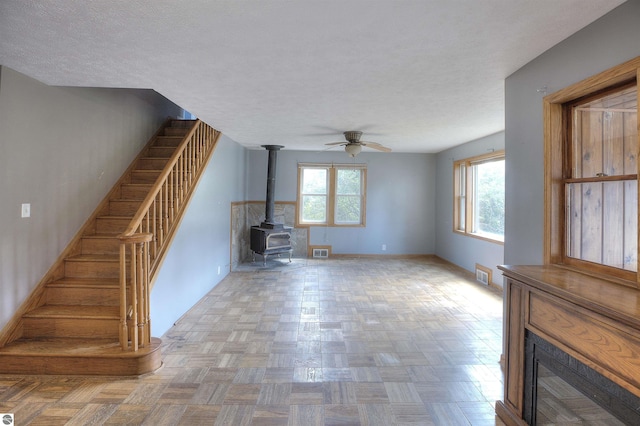 unfurnished living room with ceiling fan, a healthy amount of sunlight, a wood stove, and light parquet floors