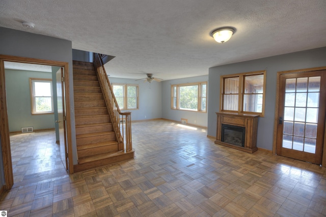 unfurnished living room featuring ceiling fan, parquet flooring, and a textured ceiling