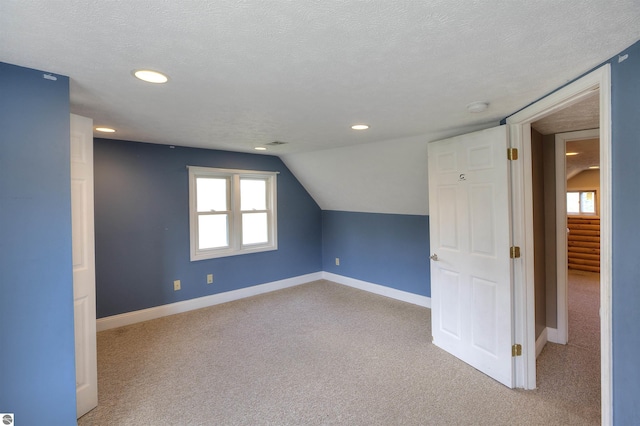 bonus room with vaulted ceiling, light carpet, and a textured ceiling