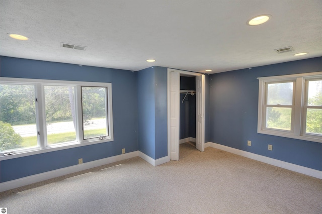 unfurnished bedroom with multiple windows, light carpet, a closet, and a textured ceiling