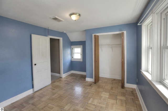 unfurnished bedroom featuring light parquet flooring, vaulted ceiling, and a closet