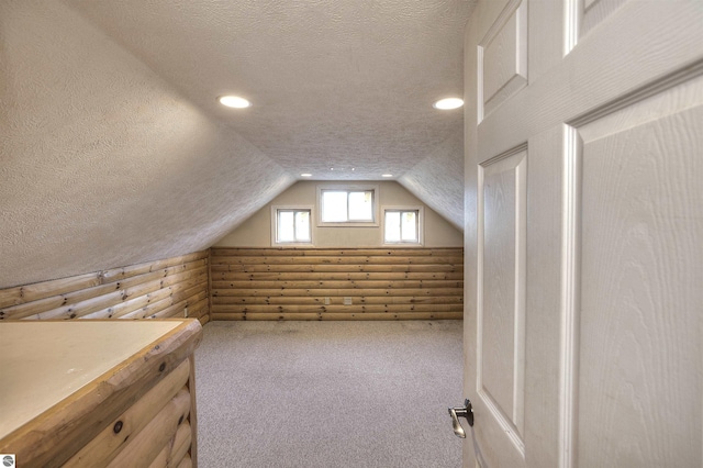 additional living space with lofted ceiling, a textured ceiling, rustic walls, and carpet flooring