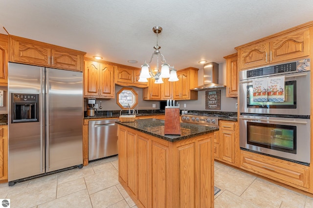 kitchen featuring light tile patterned flooring, a kitchen island, appliances with stainless steel finishes, hanging light fixtures, and wall chimney exhaust hood