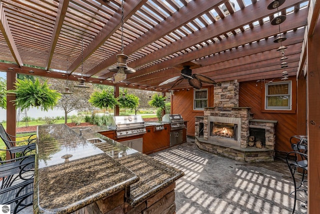 view of patio featuring area for grilling, an outdoor wet bar, an outdoor stone fireplace, and a pergola