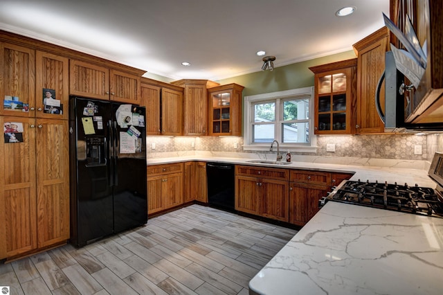 kitchen featuring sink, light stone counters, tasteful backsplash, ornamental molding, and black appliances