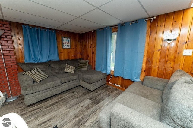 living room with hardwood / wood-style floors, a paneled ceiling, and wood walls