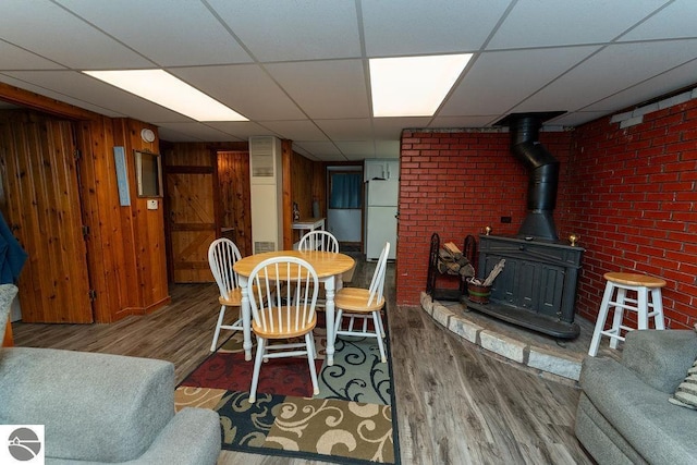 dining area featuring wood-type flooring, a wood stove, a paneled ceiling, and wood walls