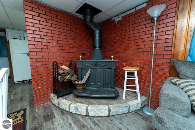 room details featuring hardwood / wood-style flooring, a paneled ceiling, white refrigerator, and a wood stove